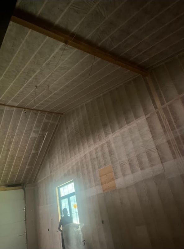 Tall vaulted room with walls and ceiling insulated behind netting, a worker standing by the window